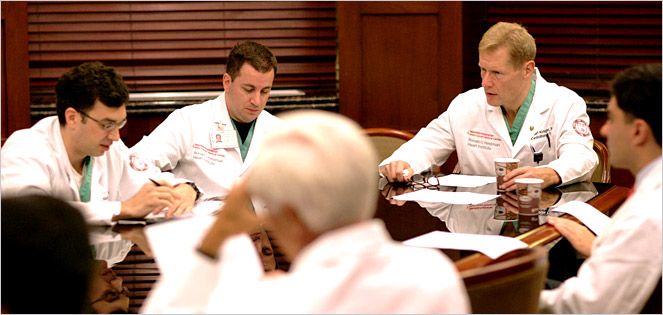 Physicians in white lab coats hold a meeting at a conference room table.